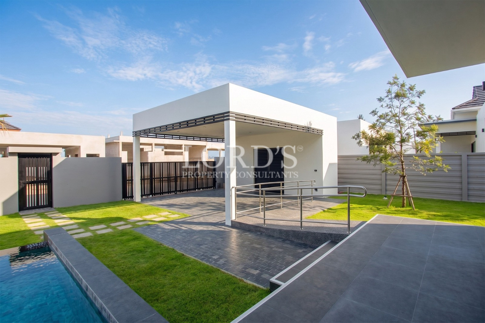 Modern luxury villa entrance with covered carport, landscaped lawn, and private pool