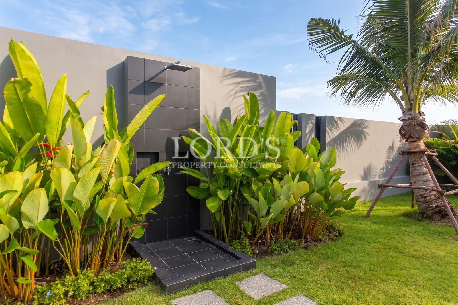 Modern outdoor shower surrounded by tropical plants and landscaped lawn