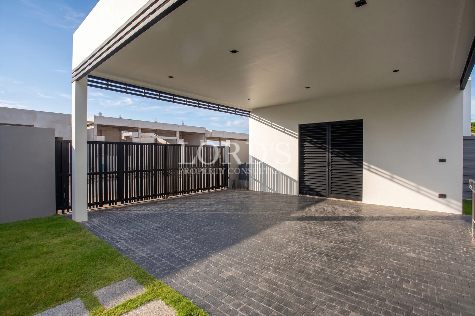 Modern villa carport with covered parking area, black gate, and landscaped lawn