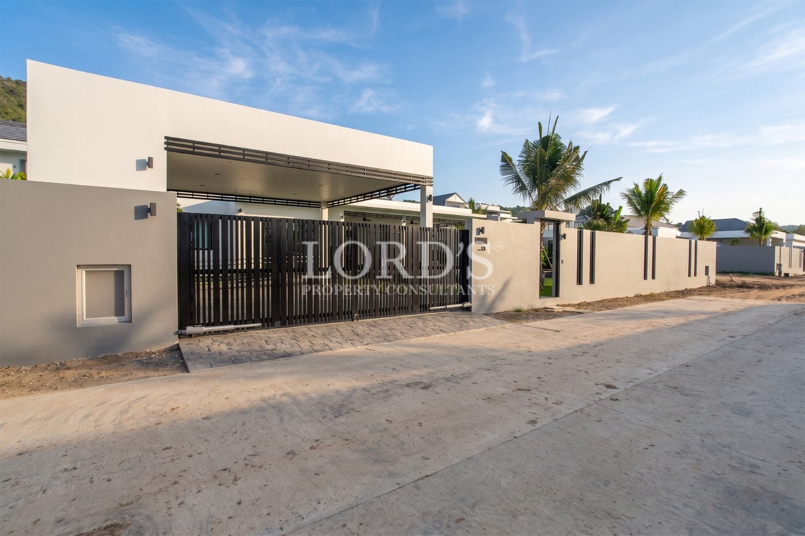 Modern villa exterior with gated entrance, covered carport, and tropical landscaping
