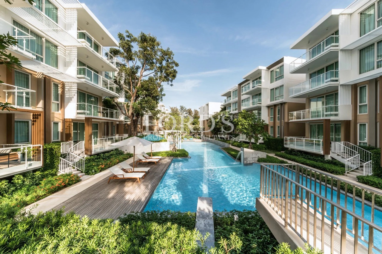 Luxury residential swimming pool surrounded by modern apartment buildings, landscaped gardens, and resort-style outdoor amenities