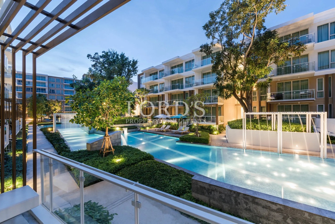Luxury apartment swimming pool with landscaped gardens, modern residential buildings, and illuminated outdoor amenities at dusk