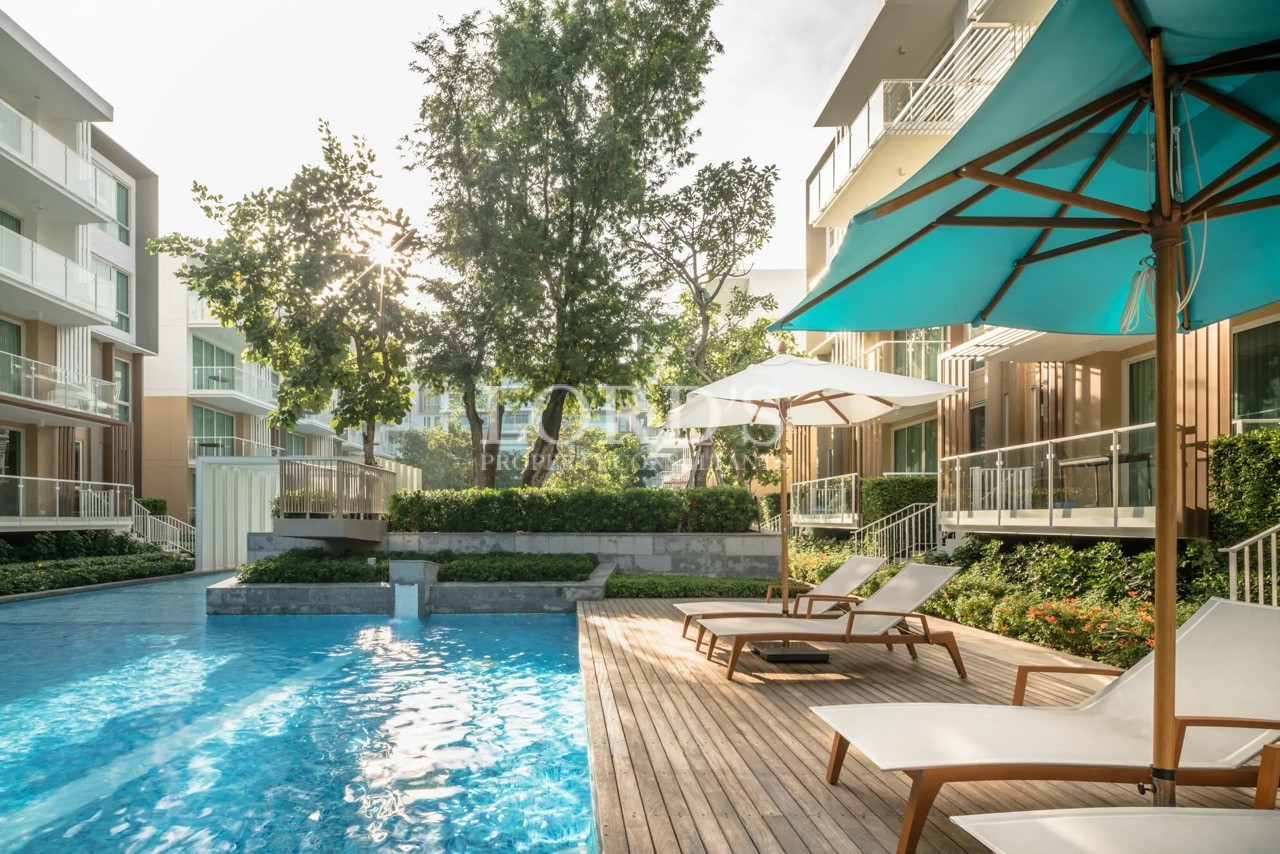 Luxury residential swimming pool with sun loungers, landscaped gardens, and modern apartment buildings