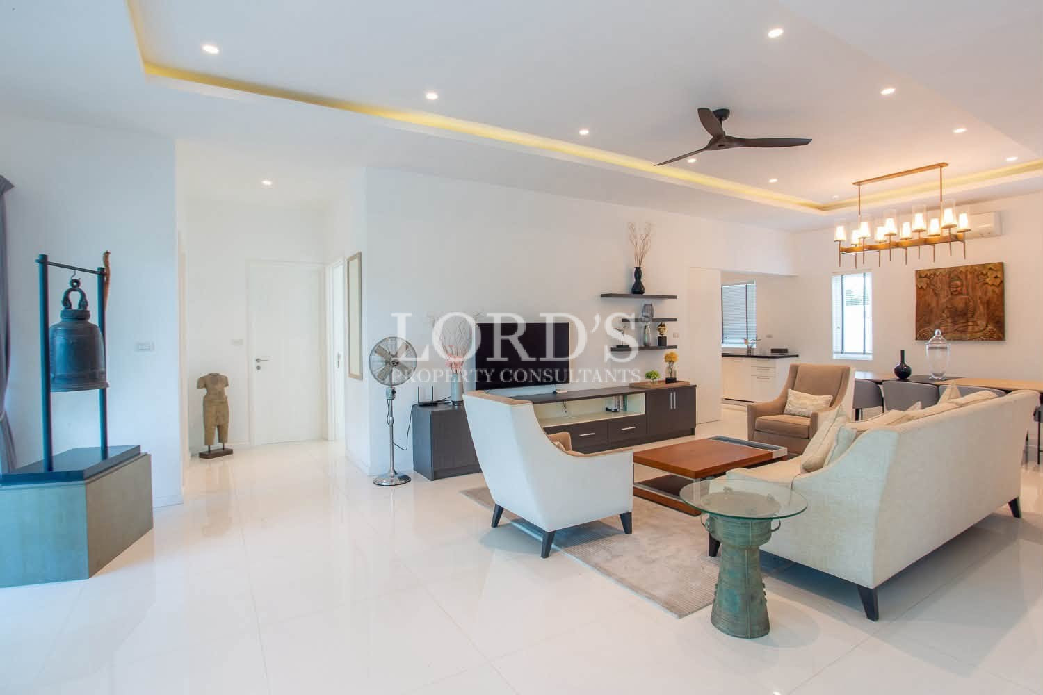 Spacious modern living room with white sofas, armchairs, TV unit, ceiling fan, and dining area