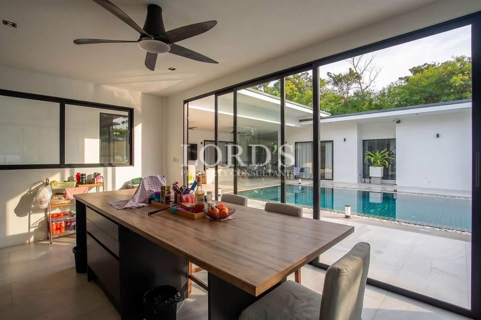 Open-plan kitchen and dining area with wooden island, large windows, and swimming pool view.