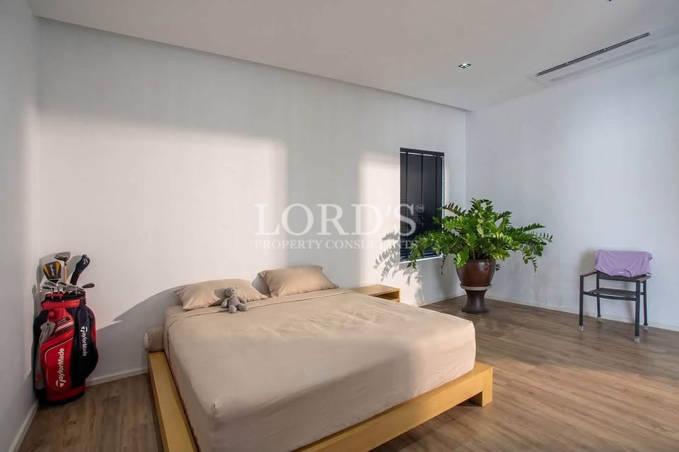Modern bedroom with a beige bed, large window, wooden flooring, and indoor plant.