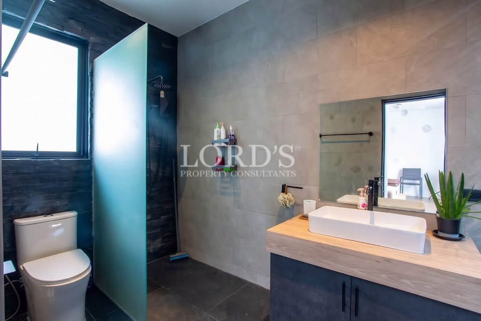 Modern bathroom with dark tiled walls, vanity, mirror, and glass shower area.