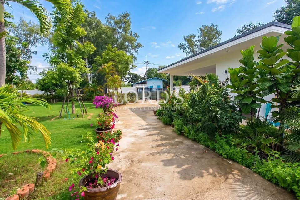Green villa garden with flowering plants, trees, and a paved walkway.