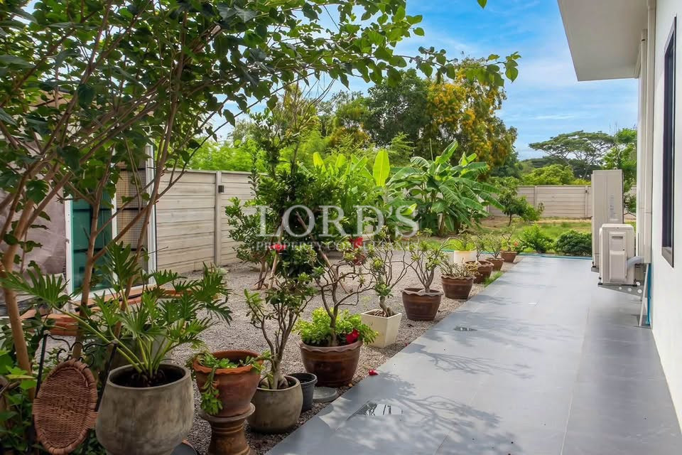Tropical garden with potted plants, flowering shrubs, and a paved walkway beside the villa.