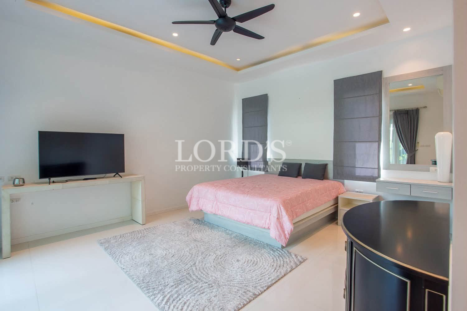 Modern bedroom with double bed, pink bedding, TV, and ceiling fan